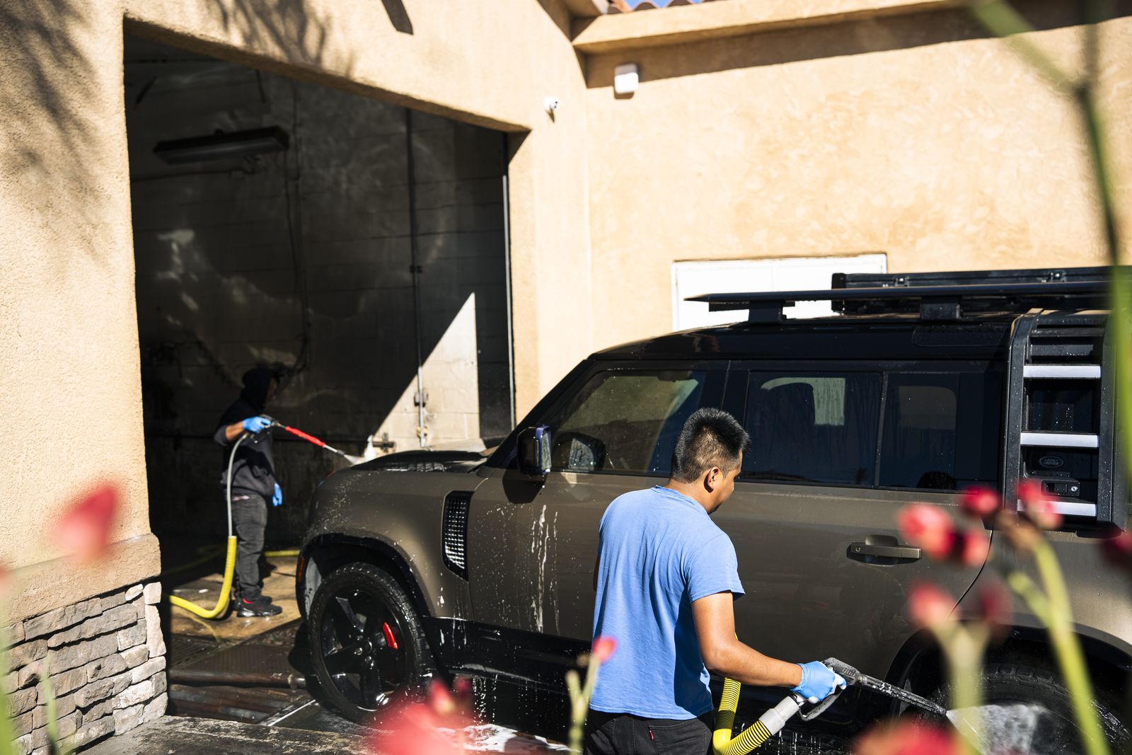 An attendant hand-washing a Land Rover Defender with a hose