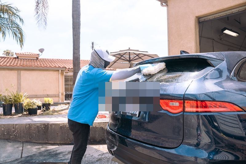 A crew member soaping the rear of a Jaguar F-Type under an umbrella