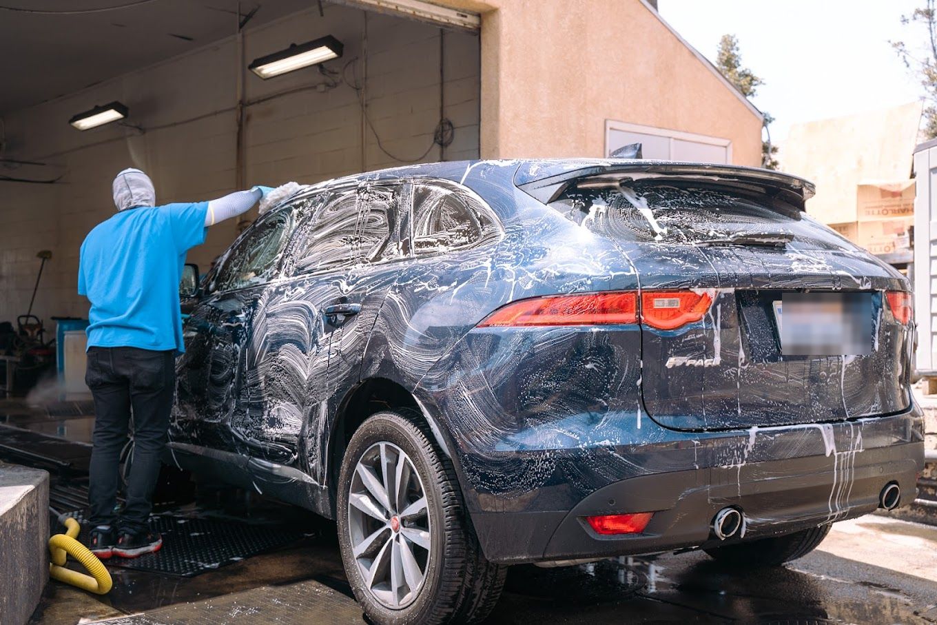 A crew member hand-washing the soaped tailgate of a navy Jaguar F-Pace