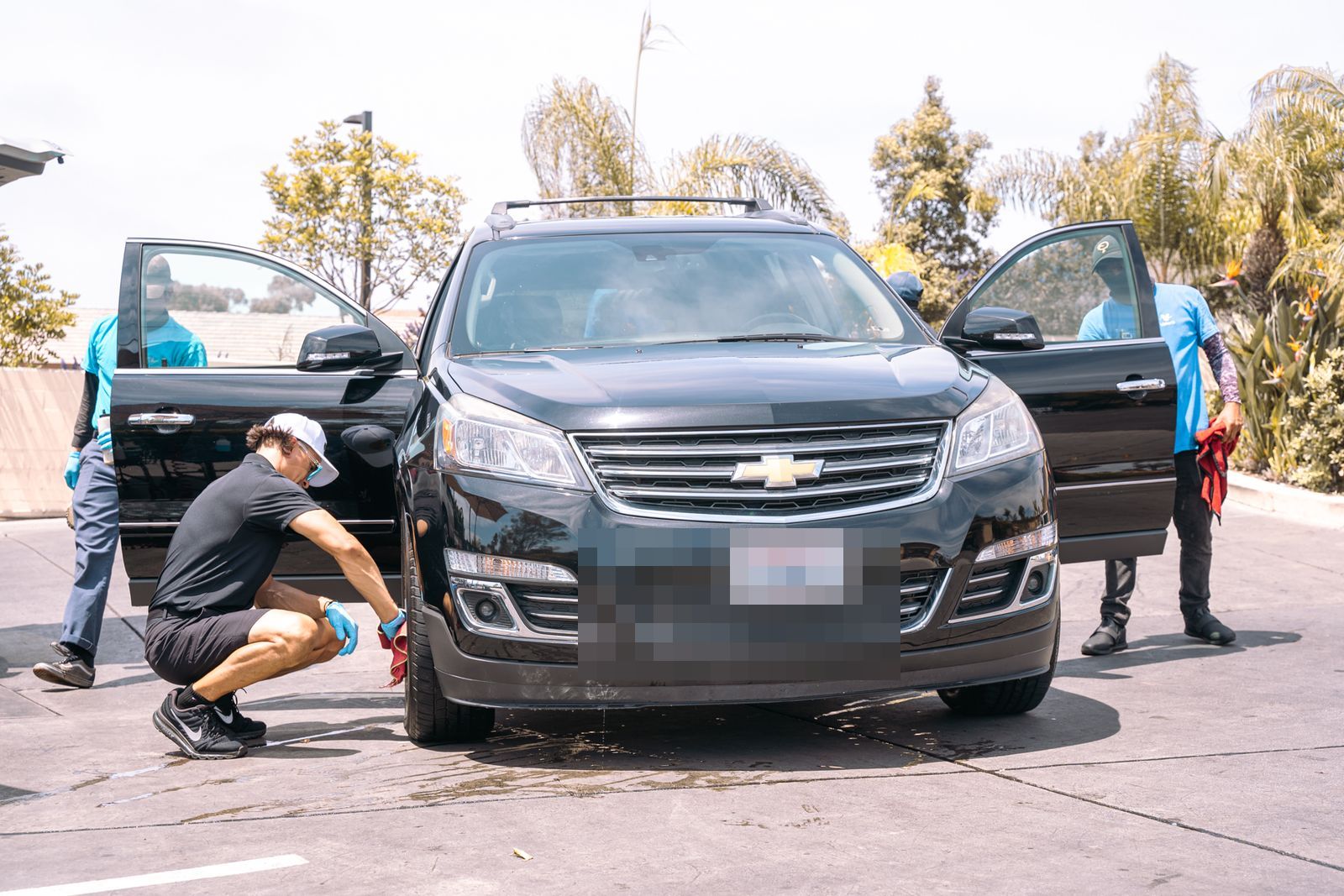 Two crew members cleaning a black Chevy Traverse with its doors open