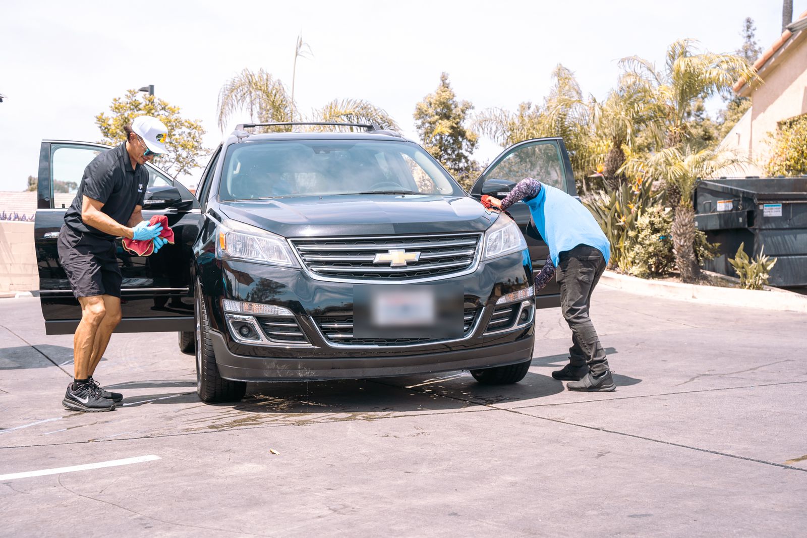 Two crew members drying a black Chevy Traverse in the lot