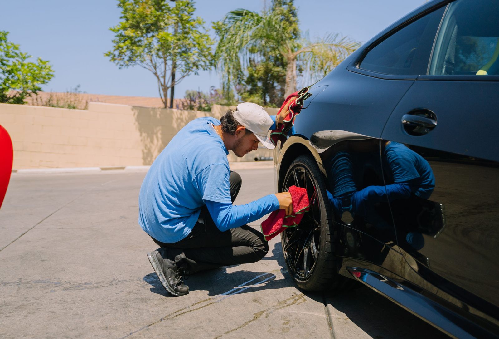 A detailer polishing the lower body panel of a dark car