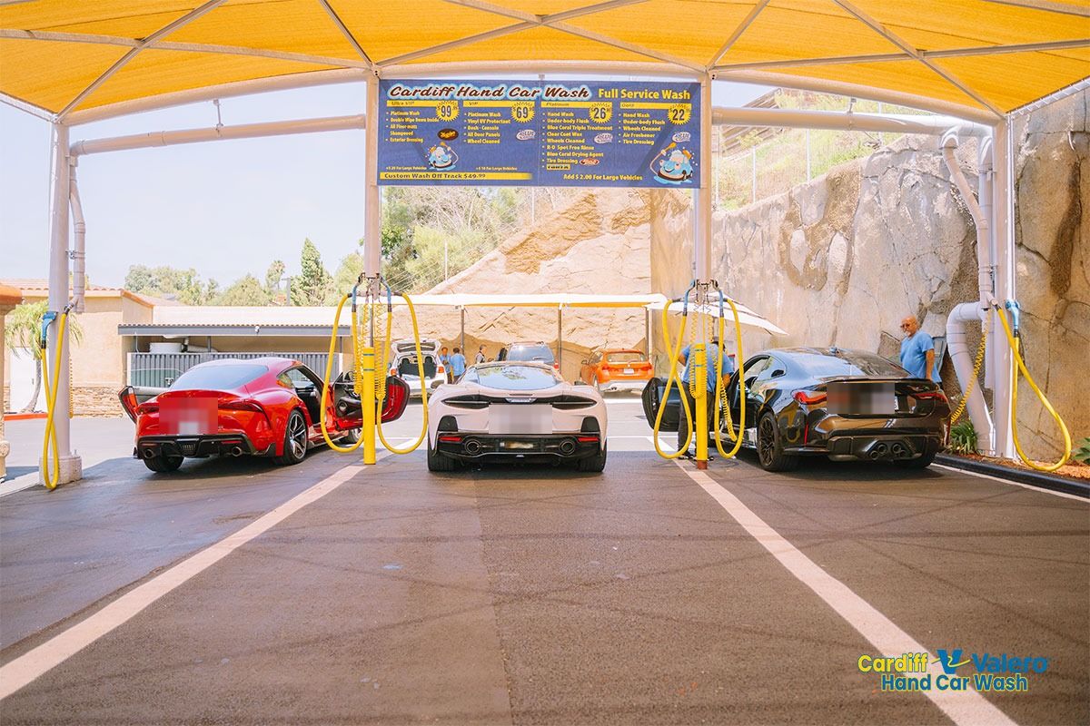 Sports cars parked under the yellow canopy beside the wash menu board